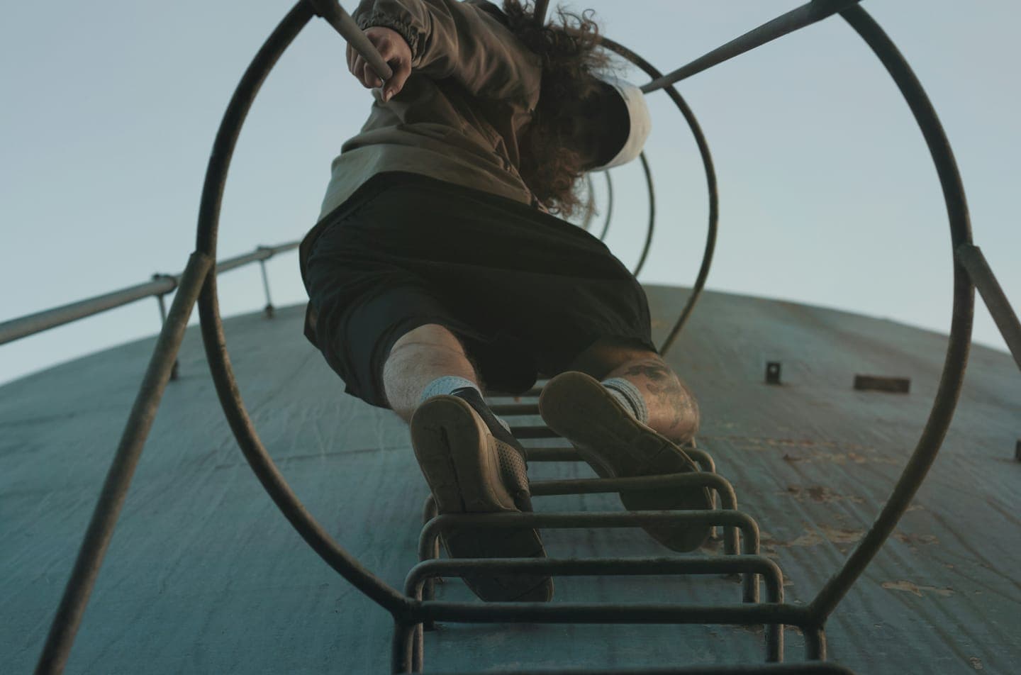 Looking up a ladder through round safety hoops at someone climbing toward the sky