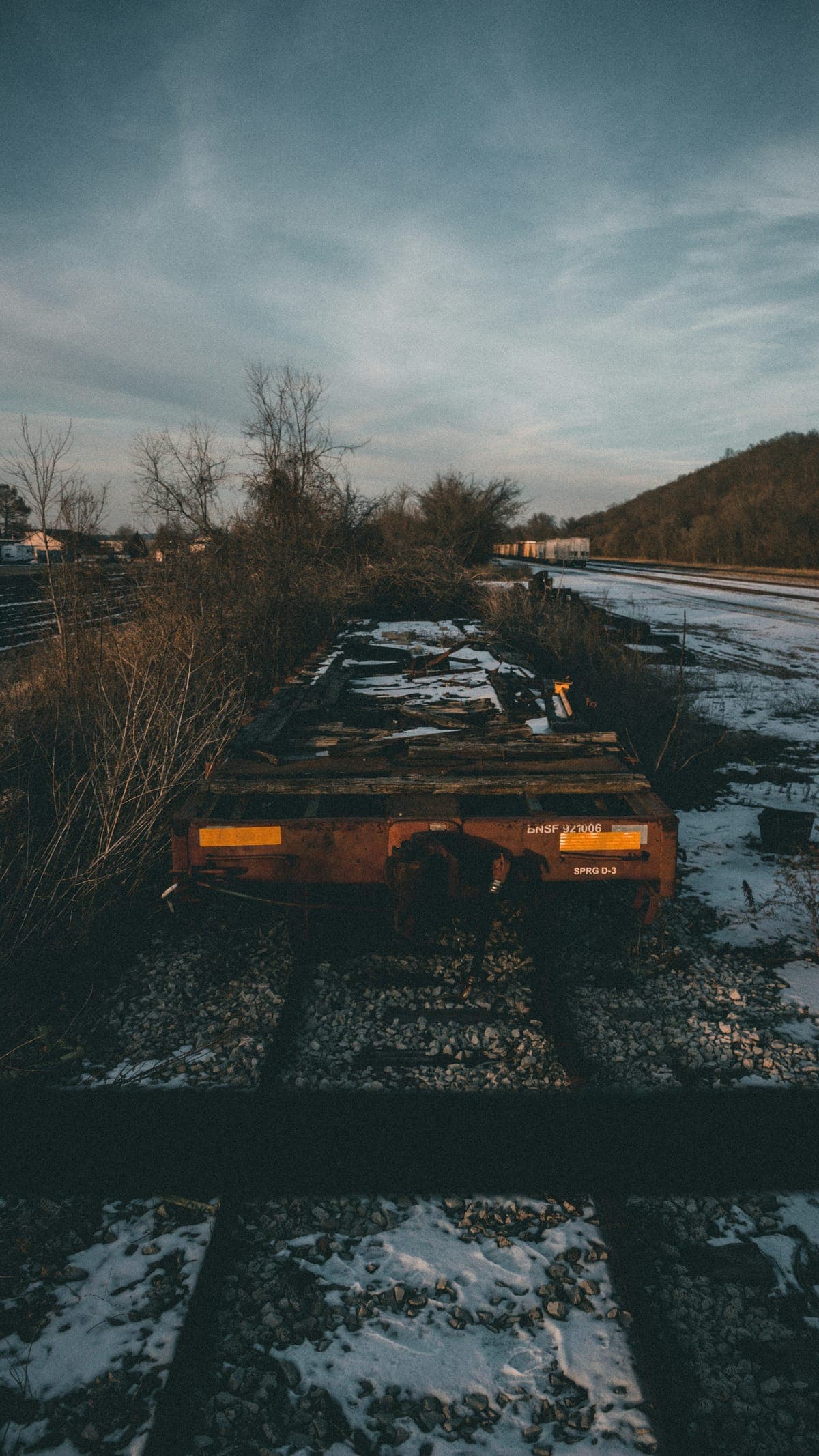 An abandoned rail car on overgrown tracks under a cloudy sky