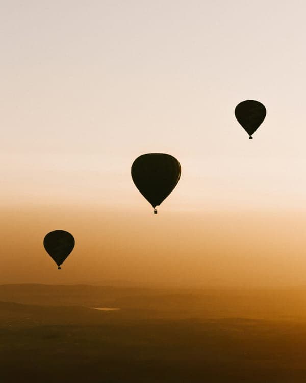 Three hot-air balloons in silhouette over a golden haze