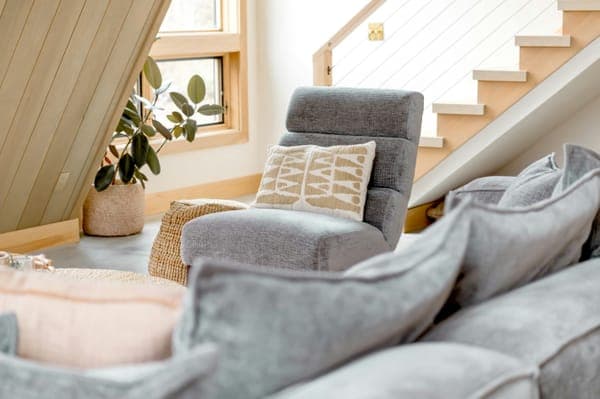 A bright attic living room with a grey sofa and an armchair under a staircase