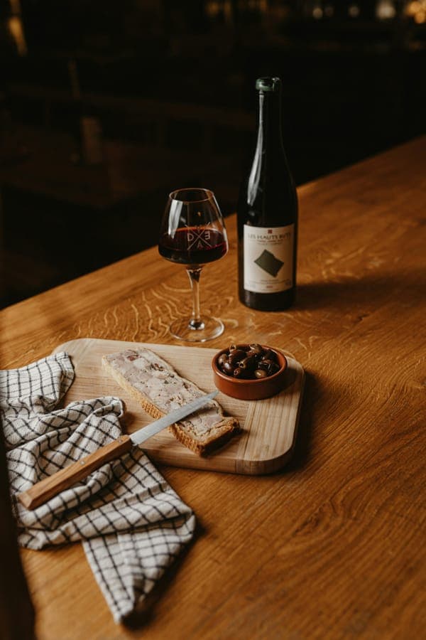 A bottle of red wine, a glass, olives and cheese on a wooden table