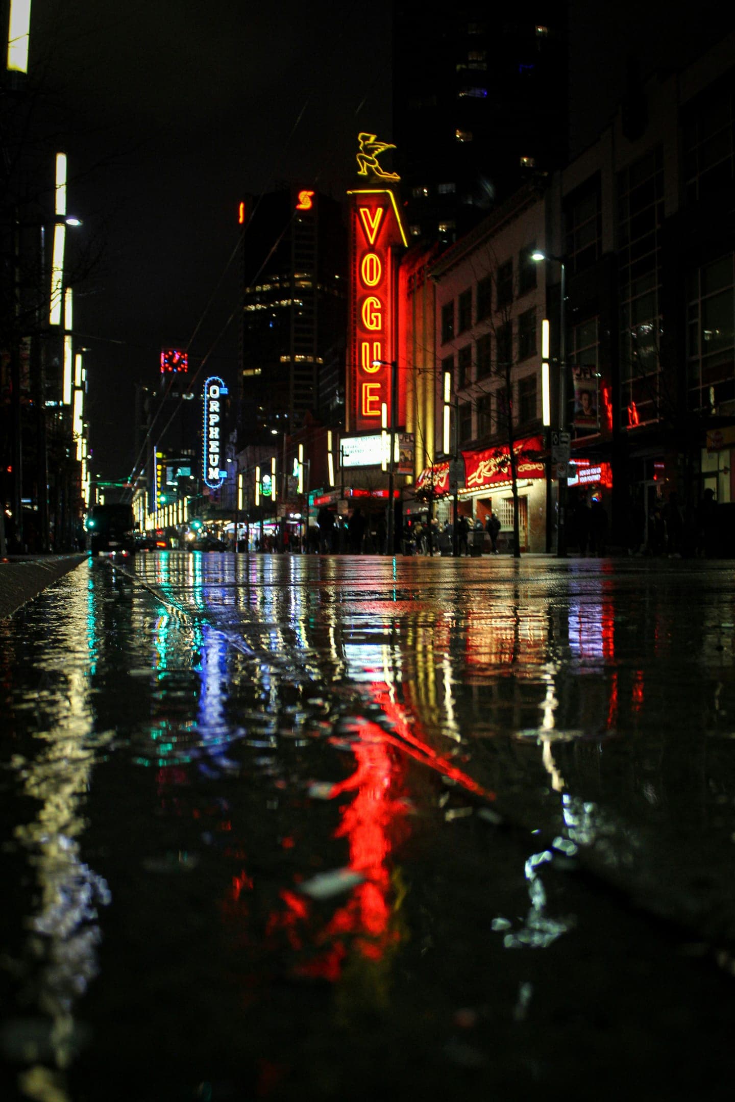 A neon sign reflected in a rain-soaked city street at night