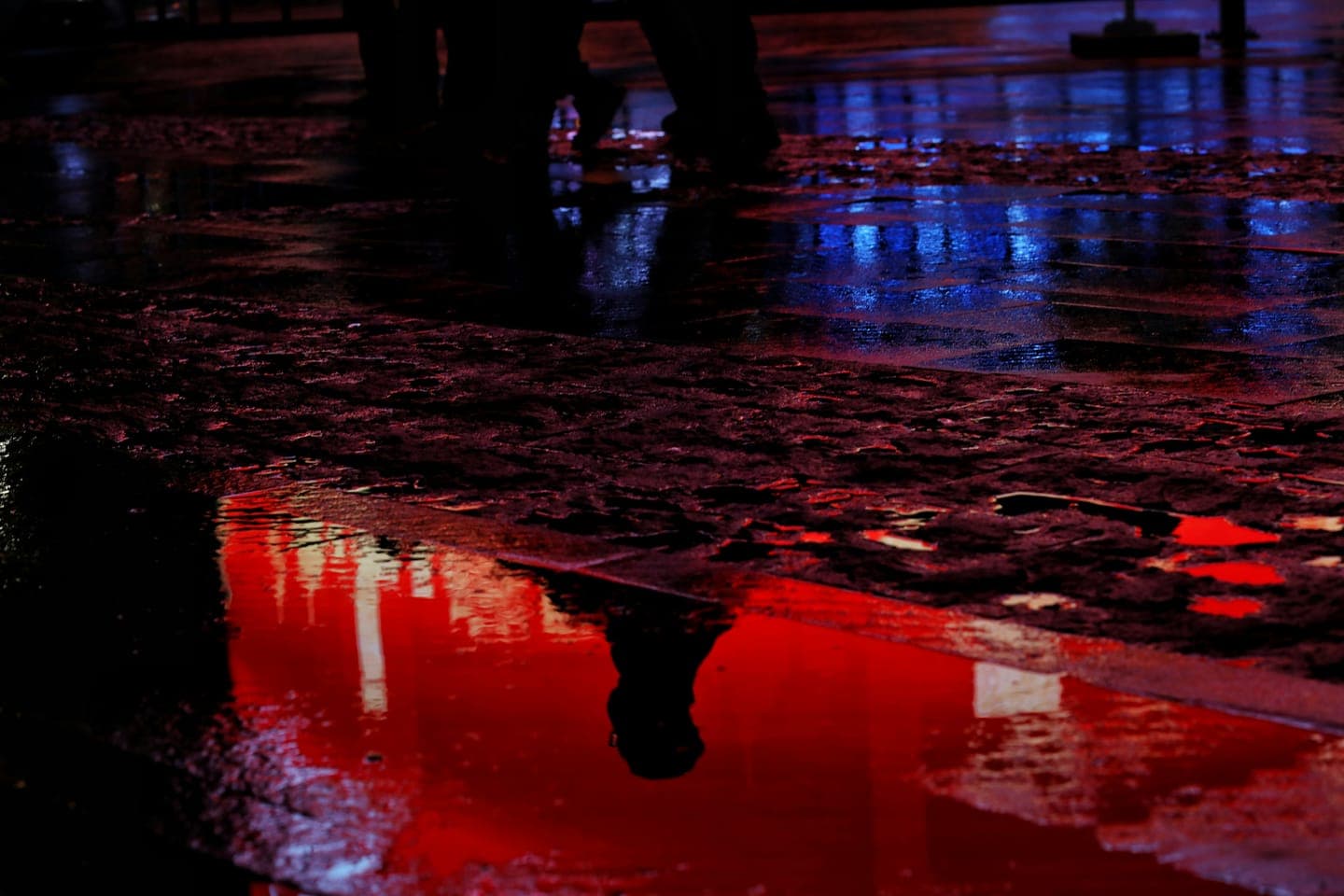 A red reflection and a passer-by in a puddle at night