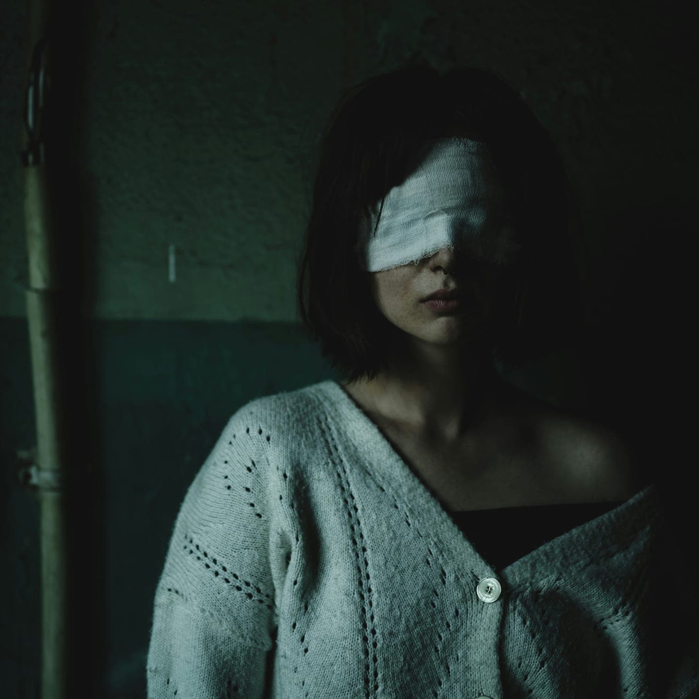 A woman in a cardigan with a white cloth over her eyes, in shadow