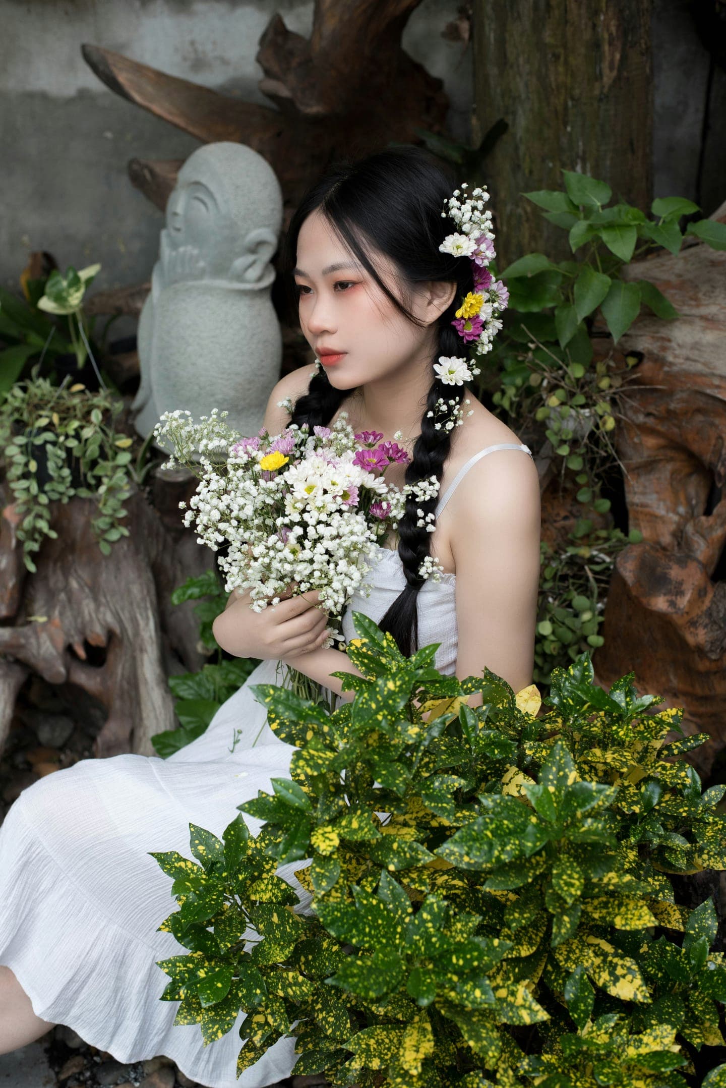 A bride in white sitting among leaves with a small bouquet