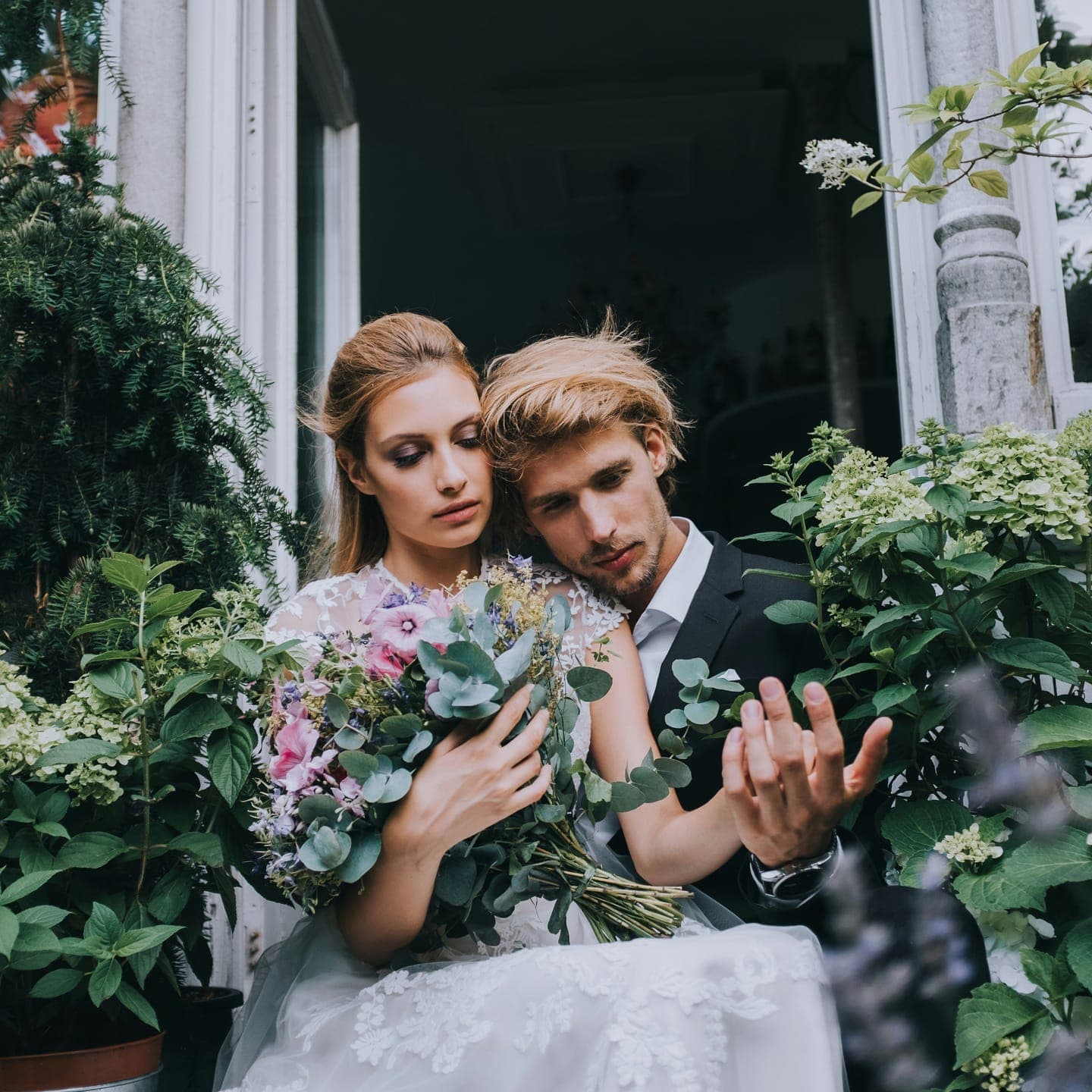 A bride and groom holding a bouquet in a doorway framed with greenery