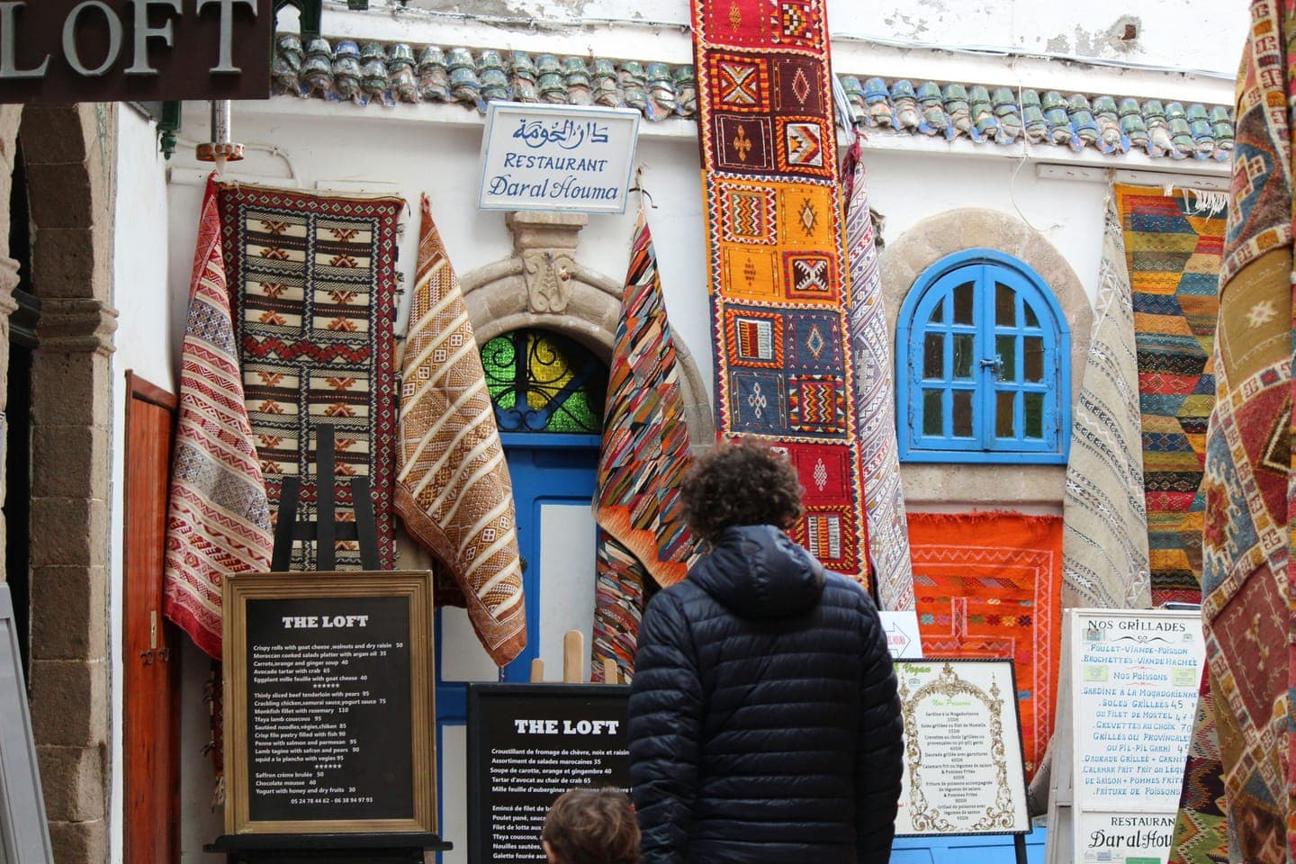 A shopper looking at rugs hung on a white shopfront