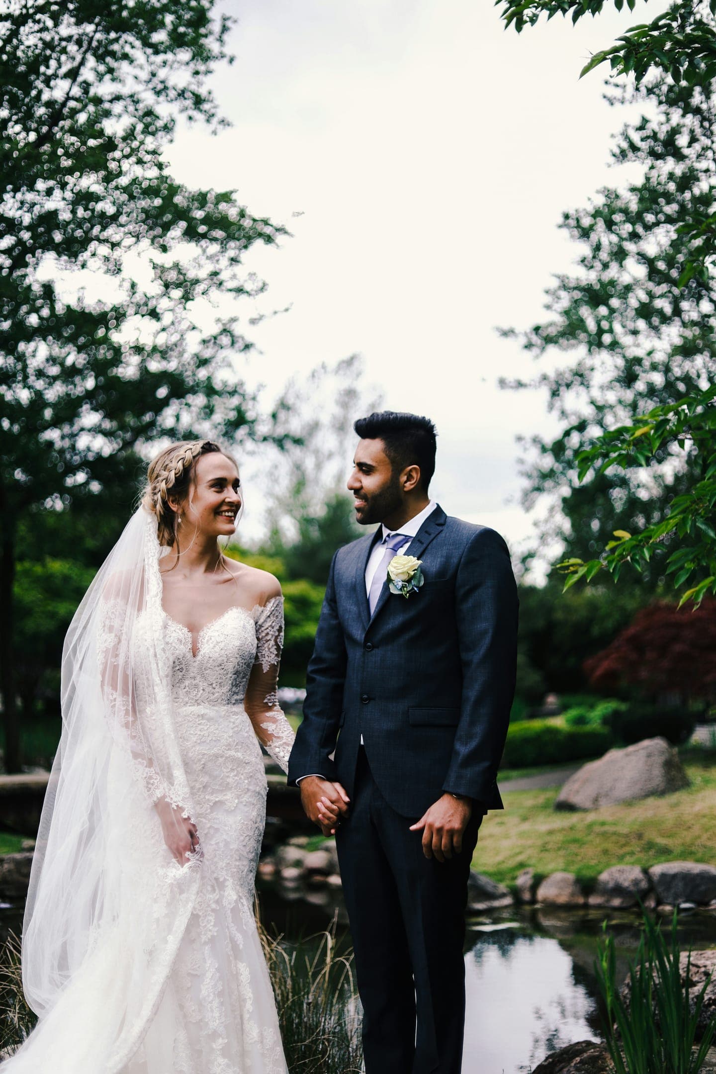 A bride and groom holding hands beside a garden pond