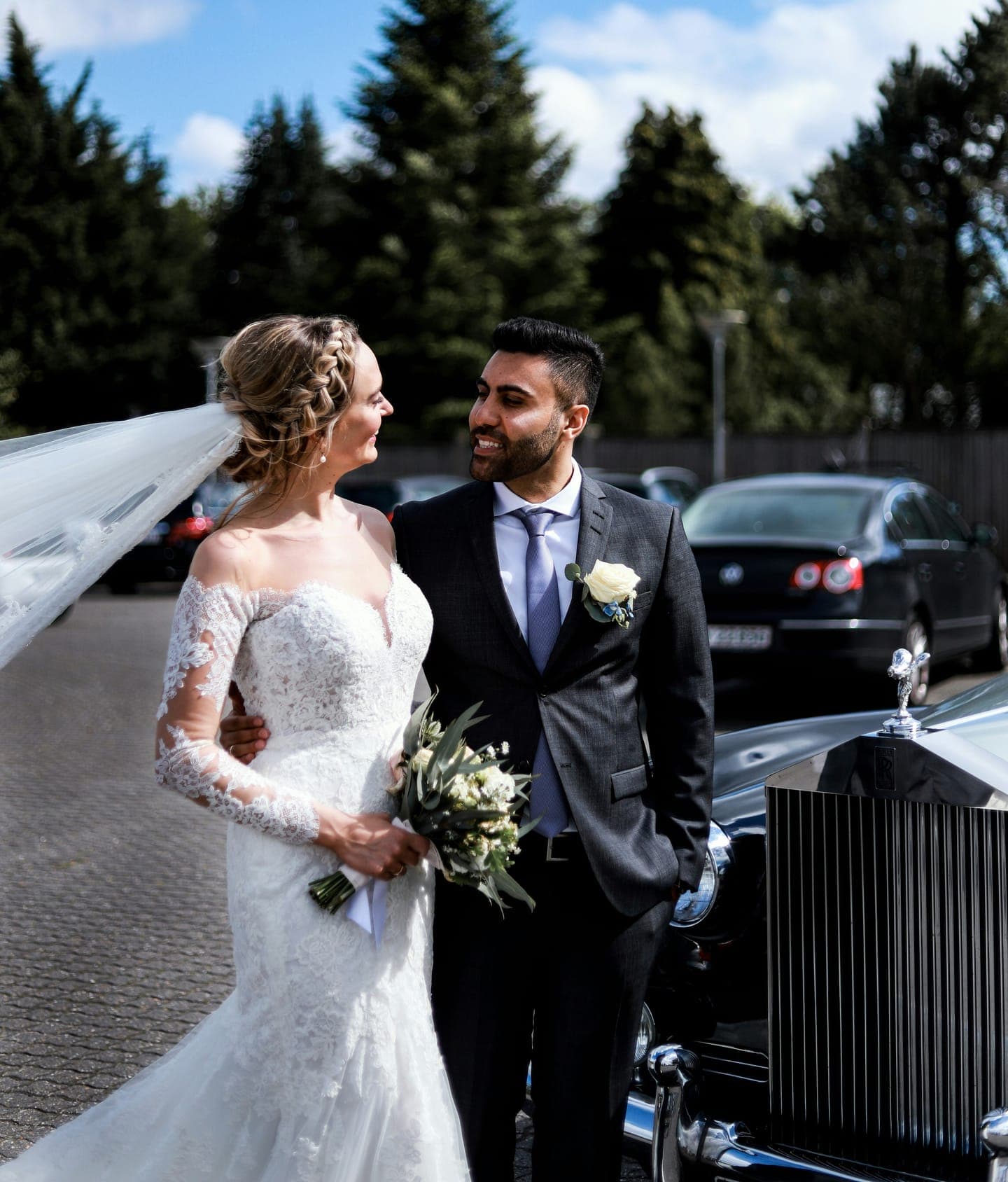A bride and groom next to a vintage car