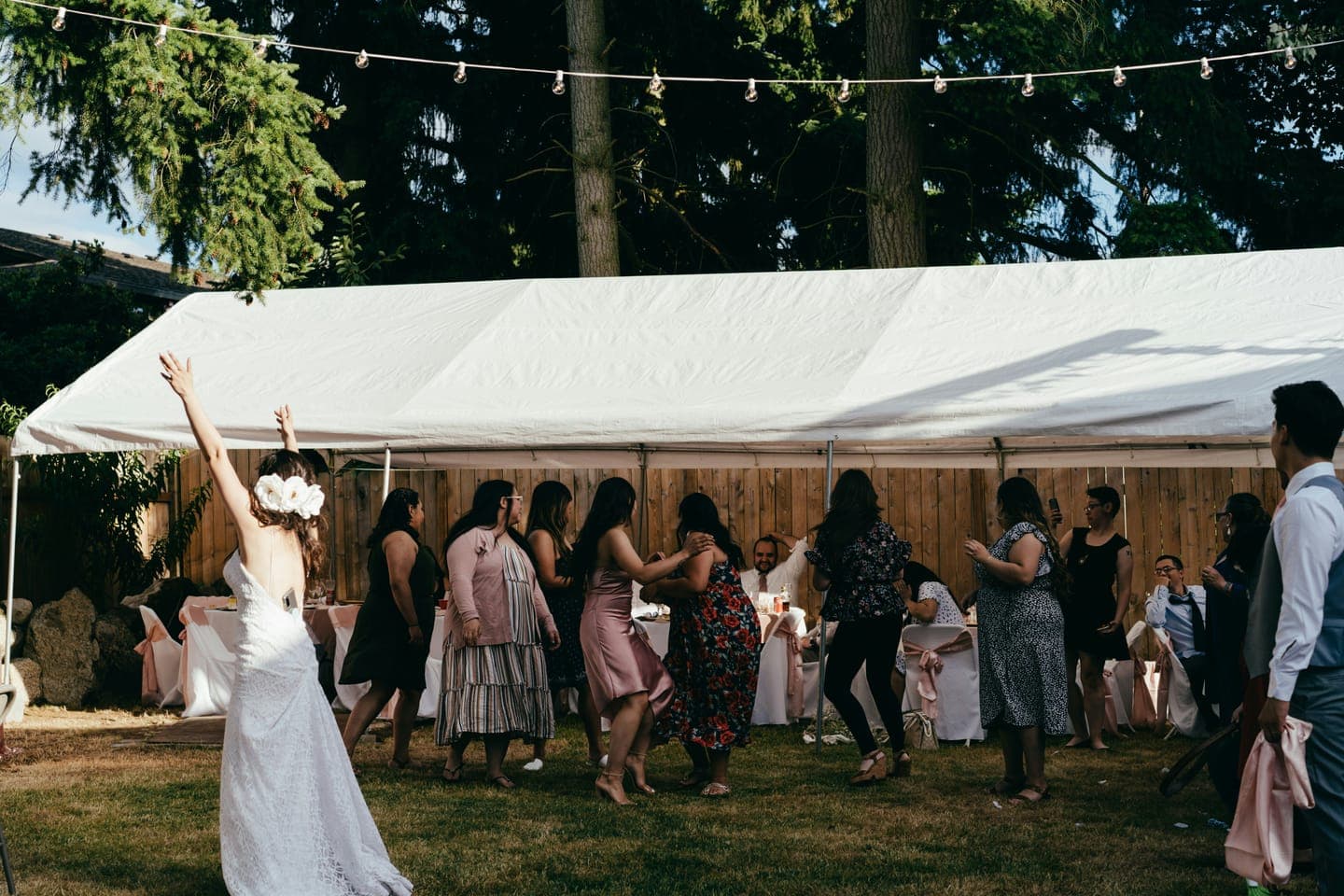 A bride dancing with guests under string lights by a tent