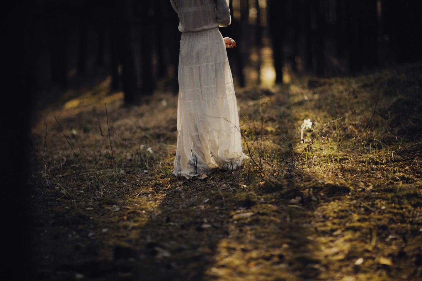 A woman in a long white dress walking through a forest