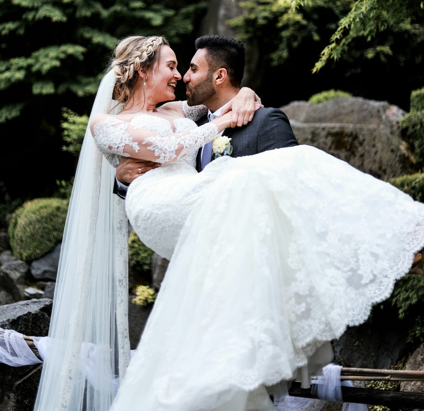 A groom carrying the bride and kissing her by a garden pond