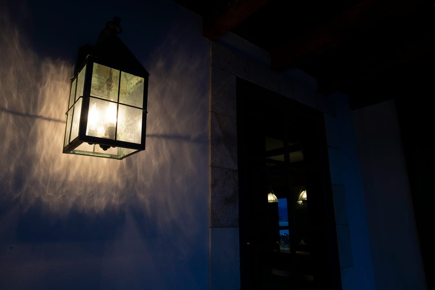 A lit wall lantern beside a doorway in the dark