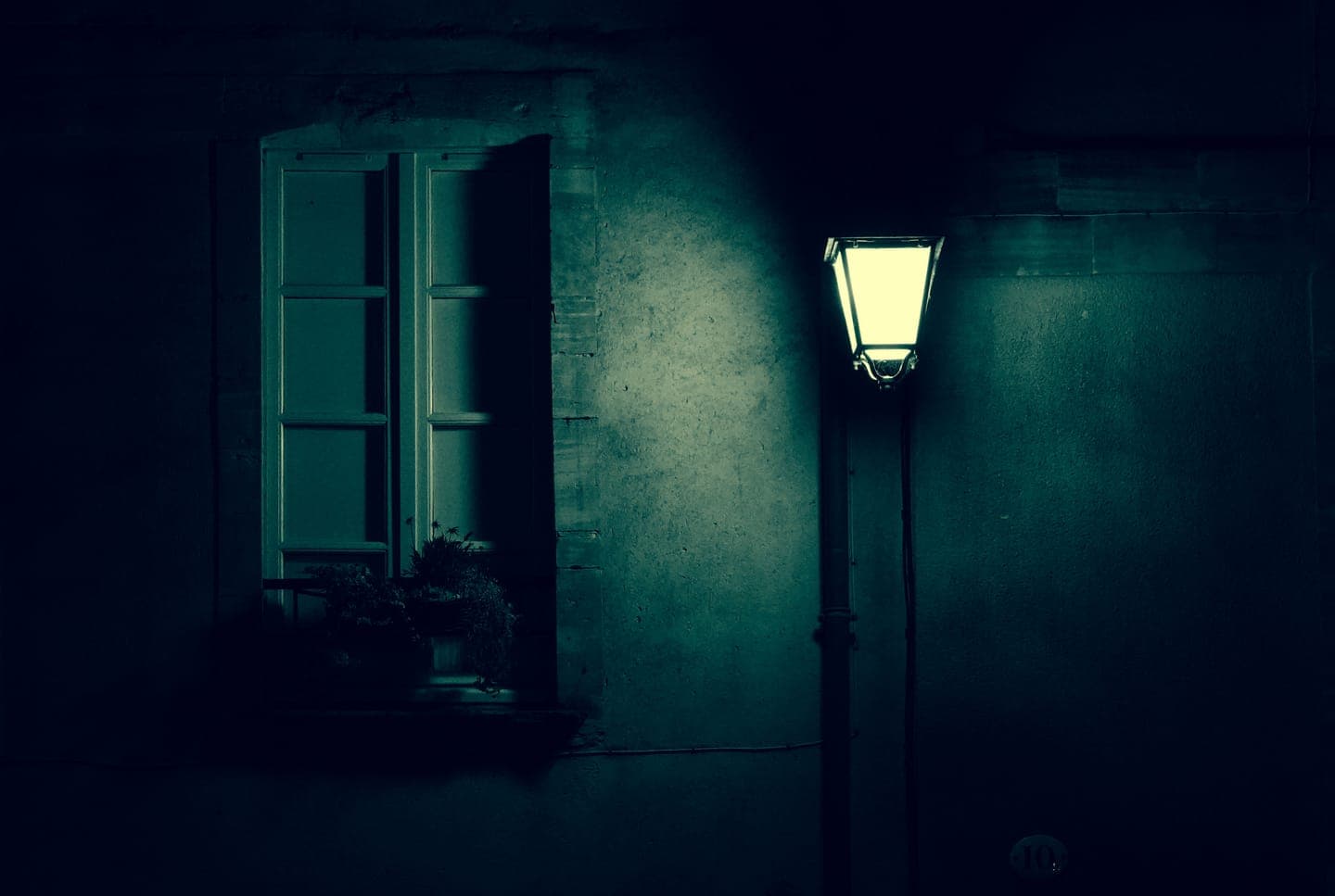 A window and a lamp post on a blue wall at dusk
