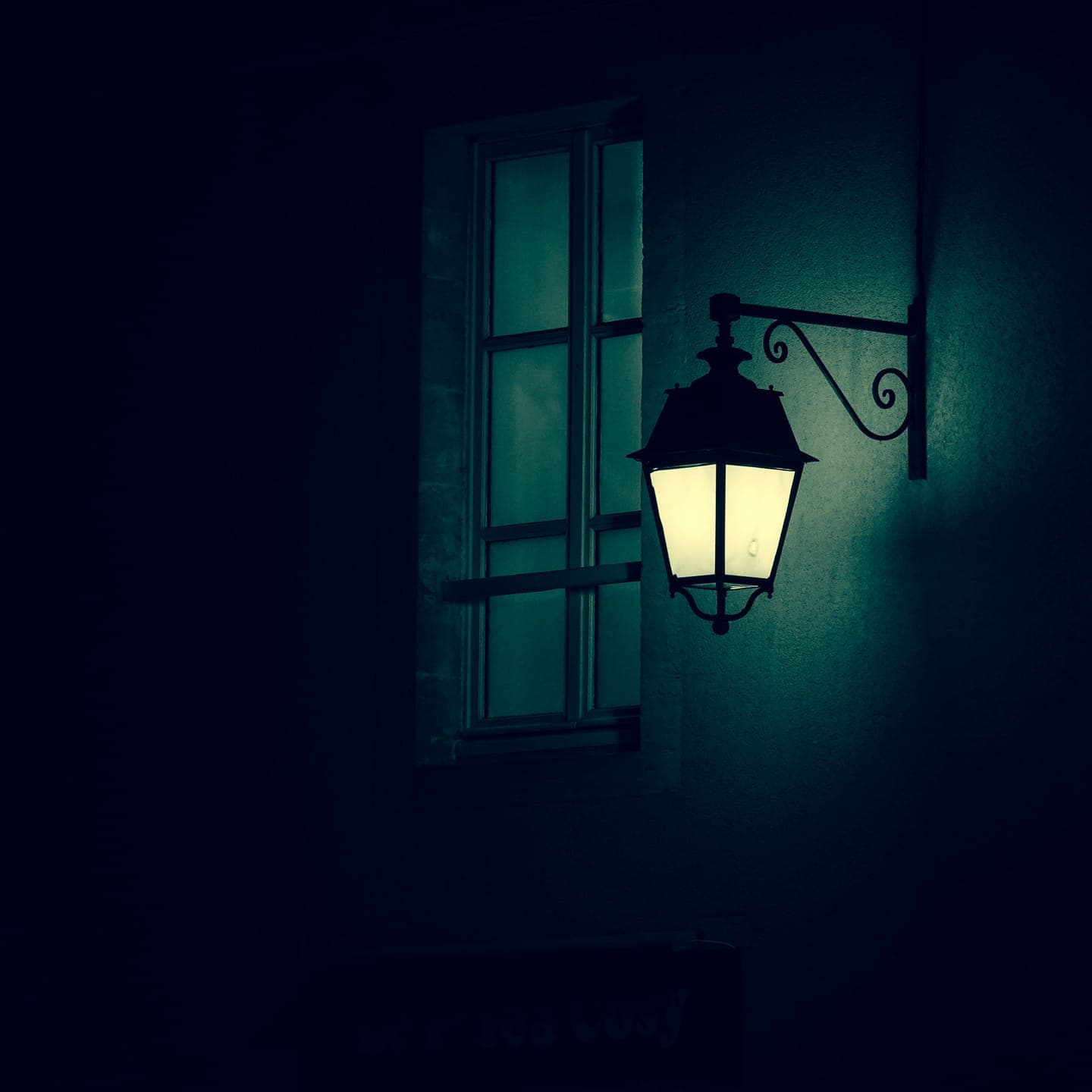 A wall lantern glowing beside a dark window at night
