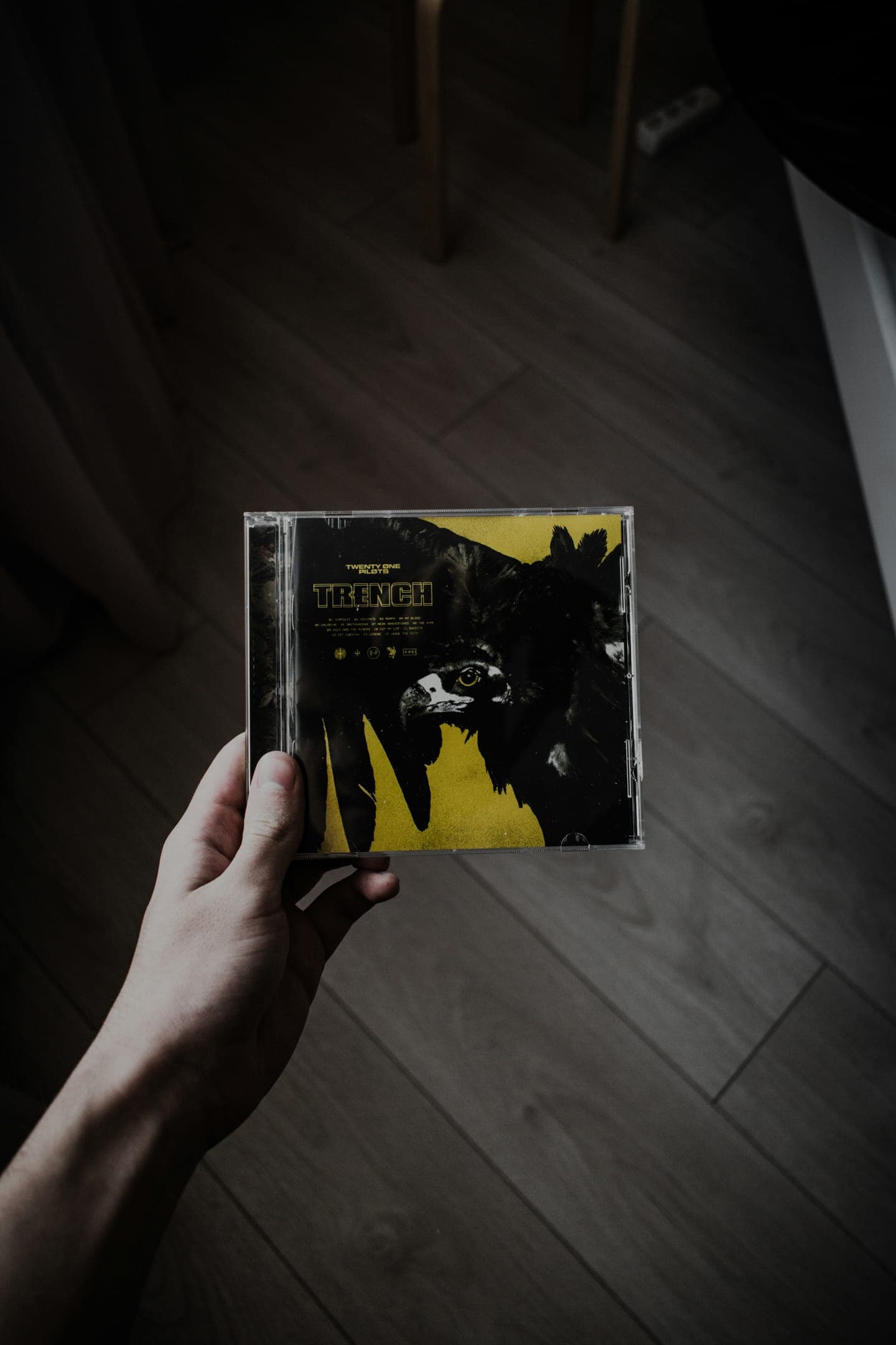 A hand holding a CD case over a wooden floor