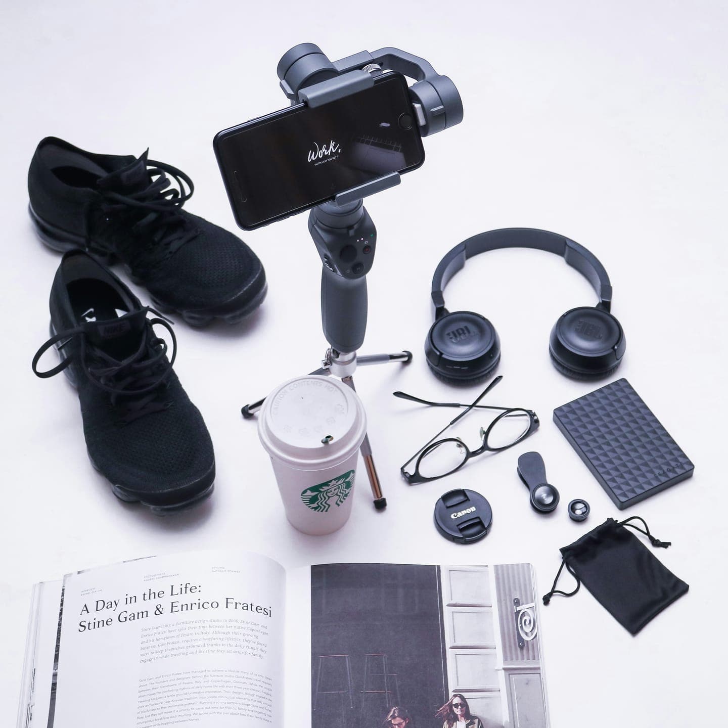 Sneakers, headphones, a phone on a gimbal and a magazine laid out on white