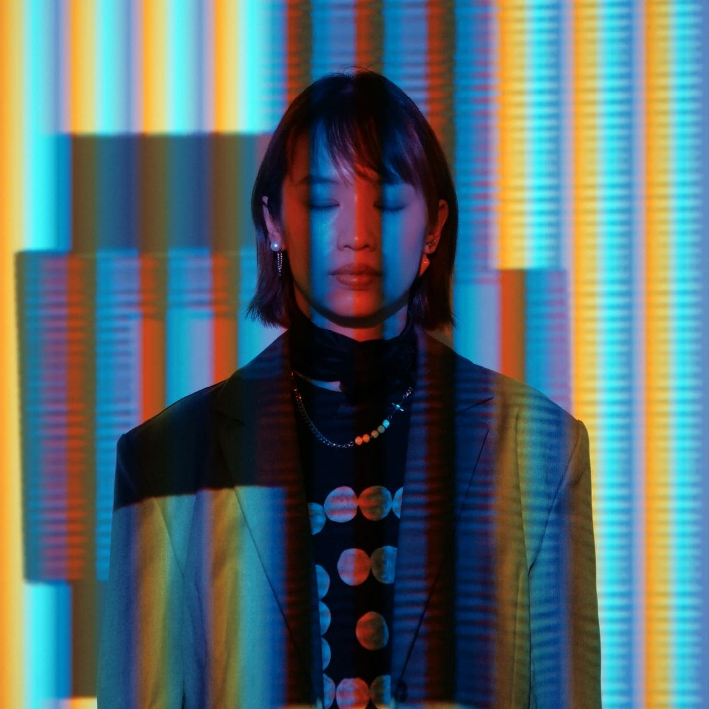 A woman with eyes closed in front of a wall of coloured light