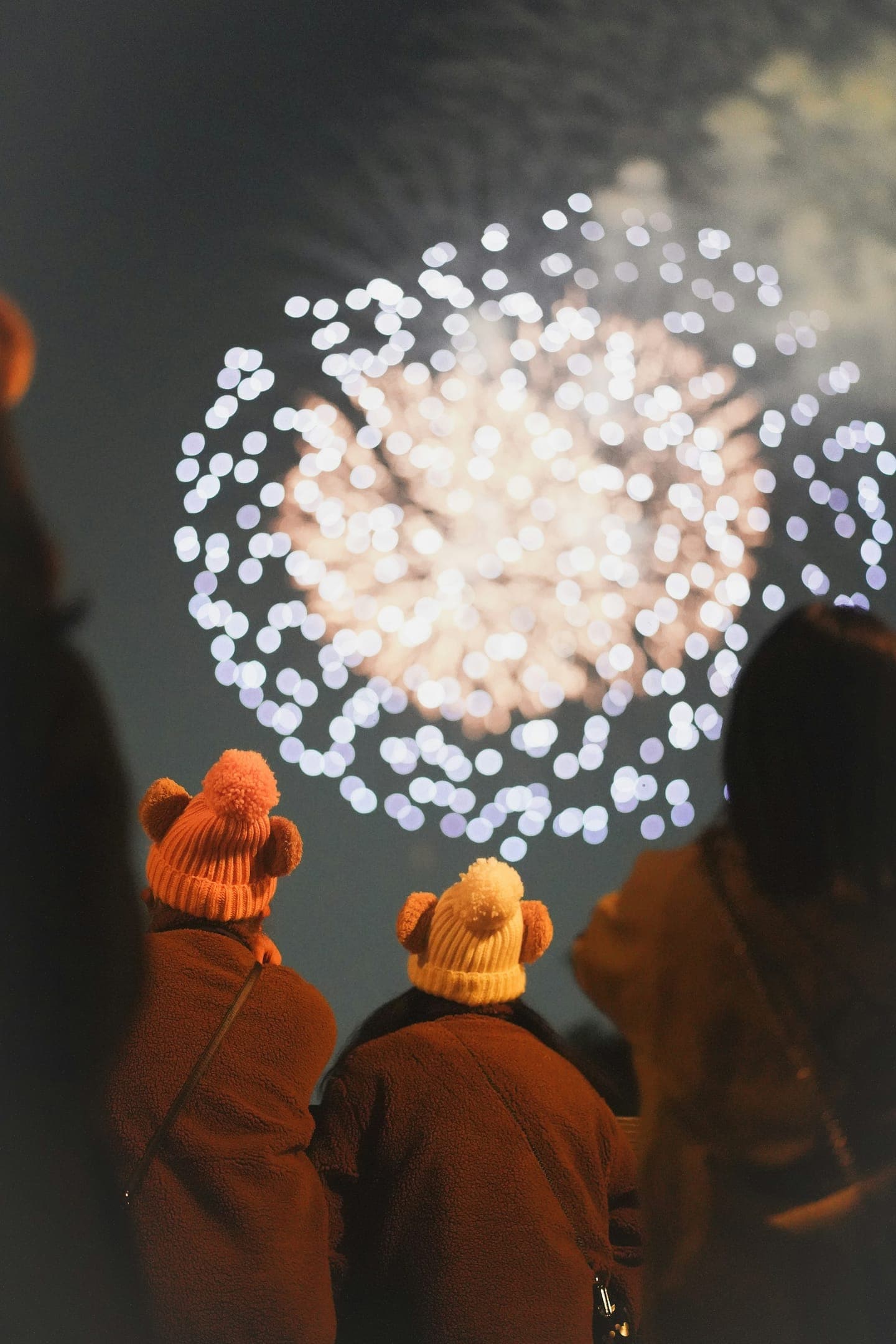 Three people in knitted hats watching fireworks
