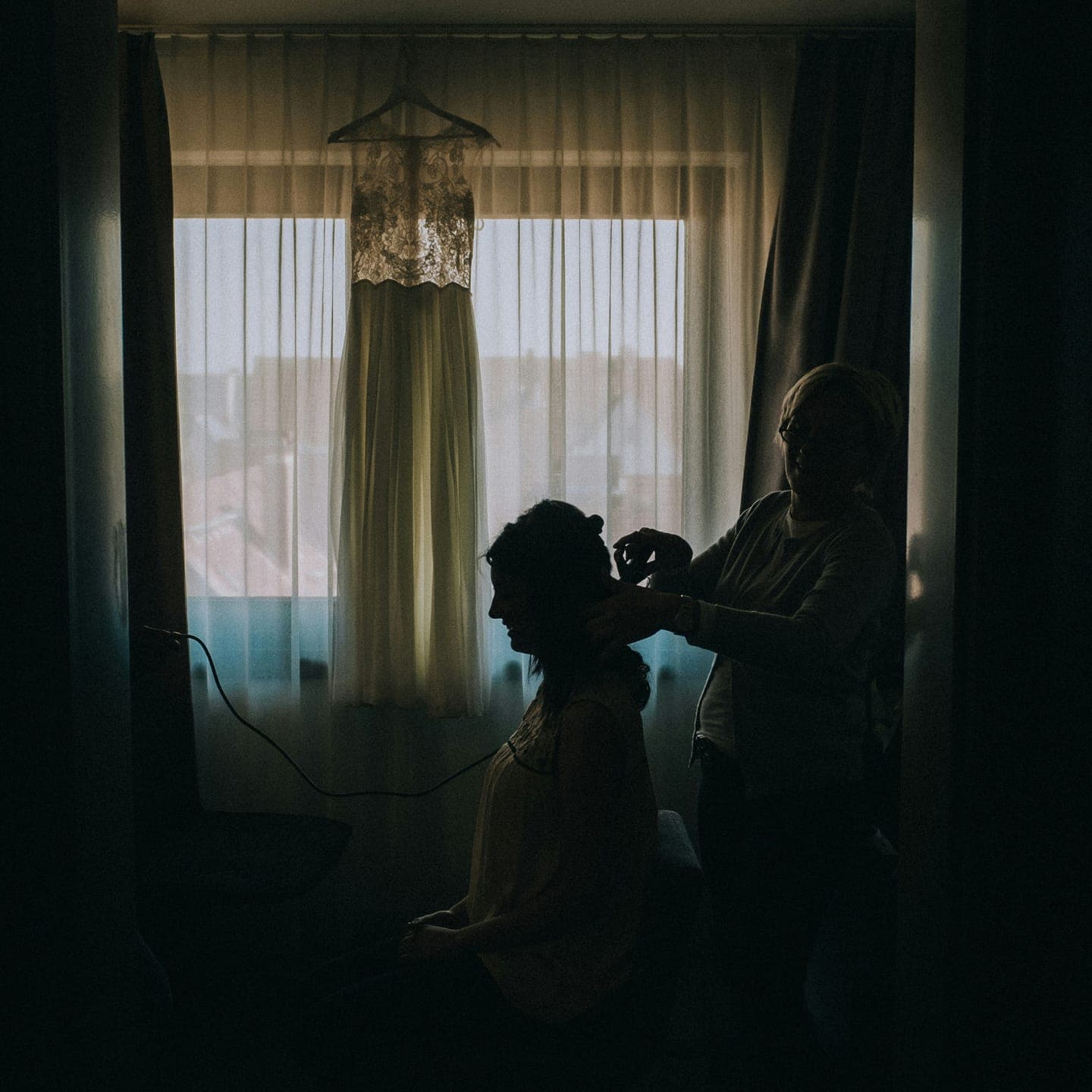 A bride having her hair done by a window in the morning