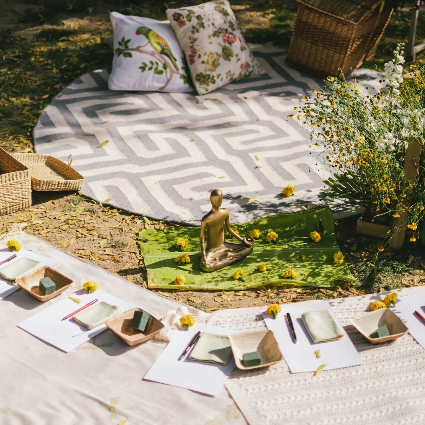 A patterned rug with cushions, a basket and place settings outdoors