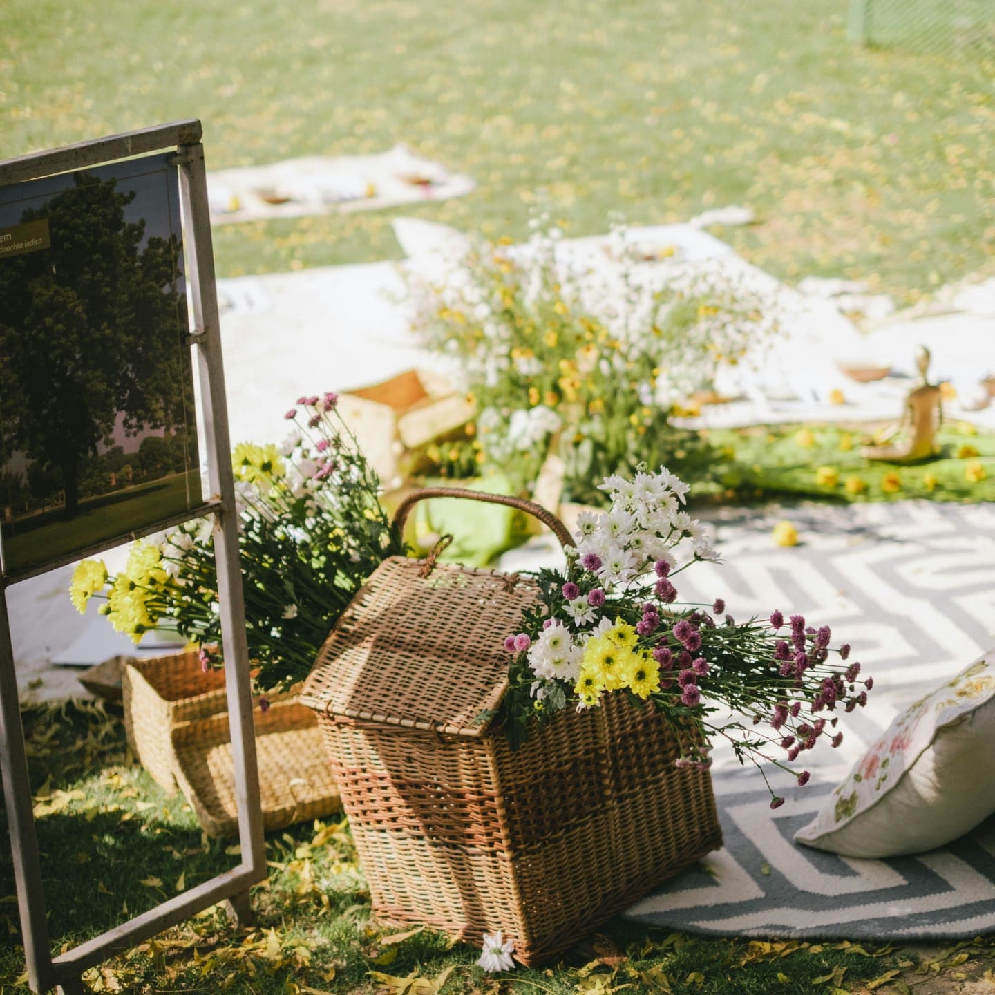 A wicker basket of flowers and a mirror on a picnic rug in a meadow