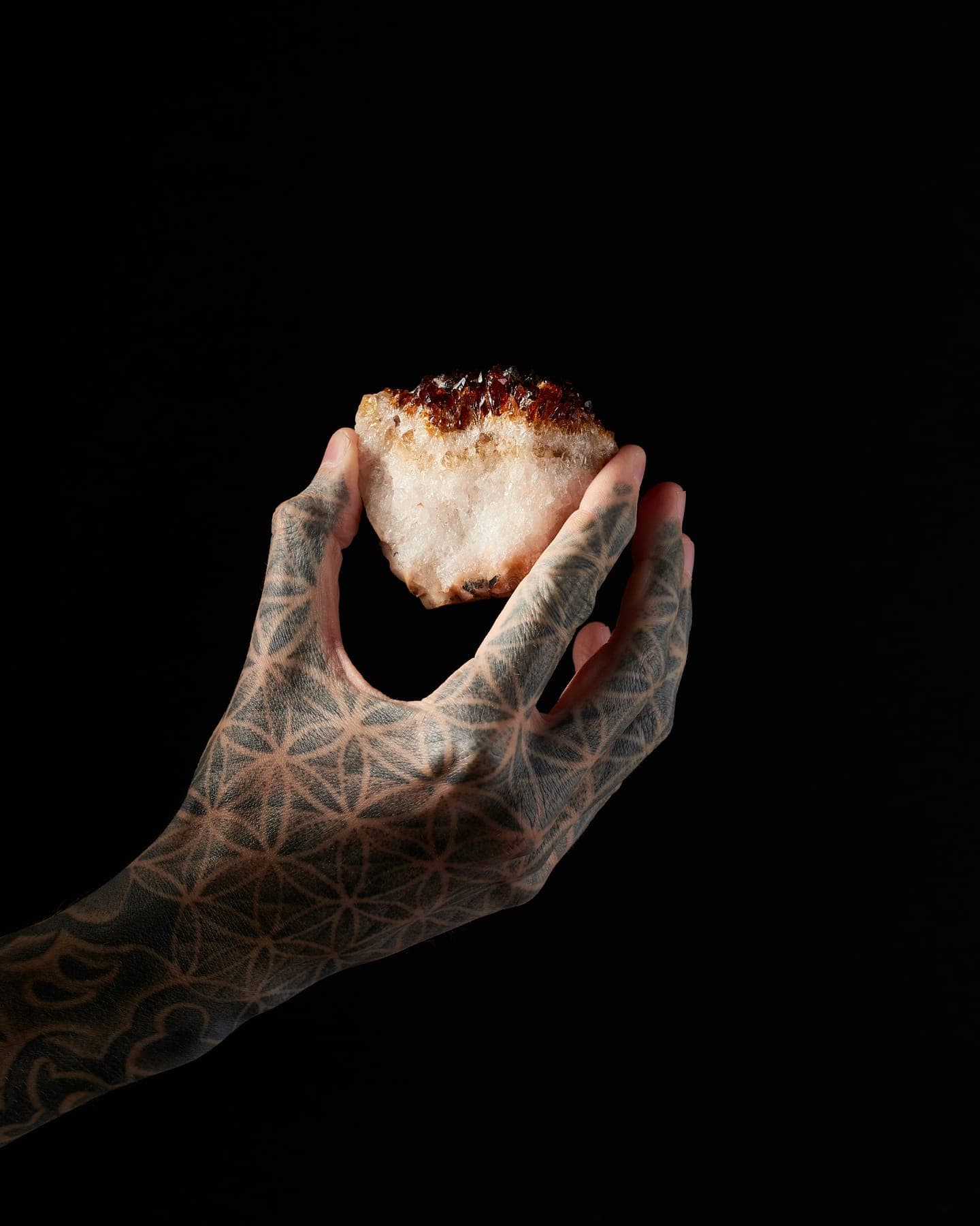 A tattooed hand holding a crystal against black