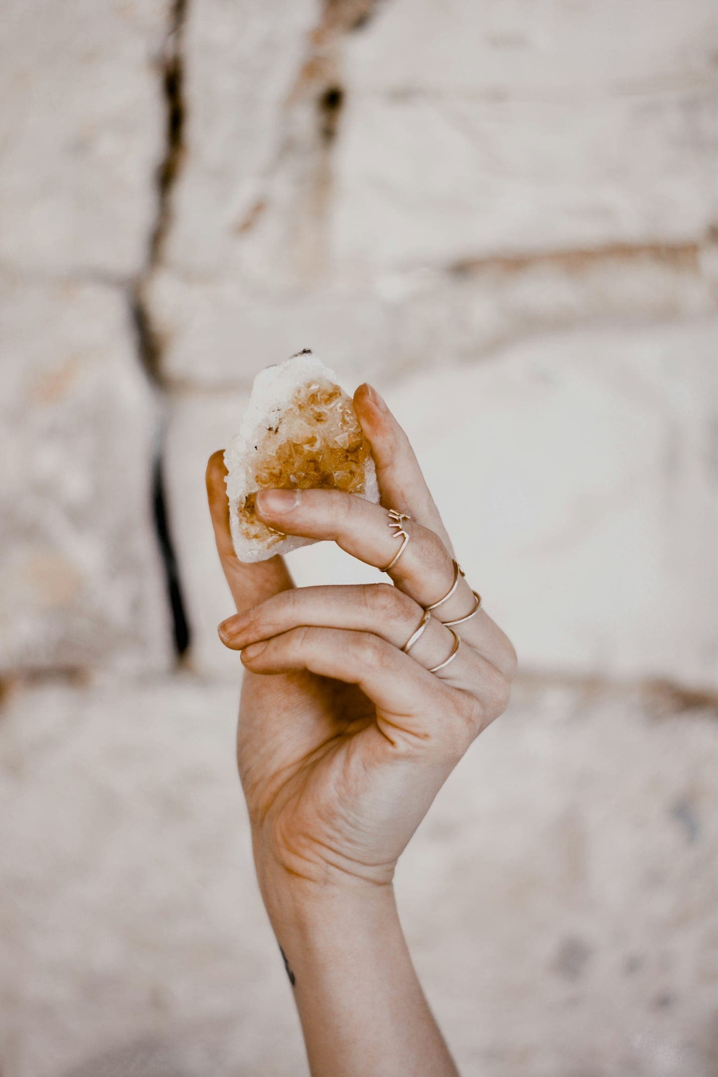 A hand holding a crystal against a pale stone wall