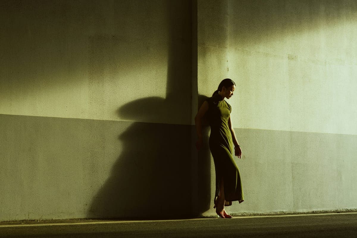 A woman leaning against a sunlit wall with her shadow beside her