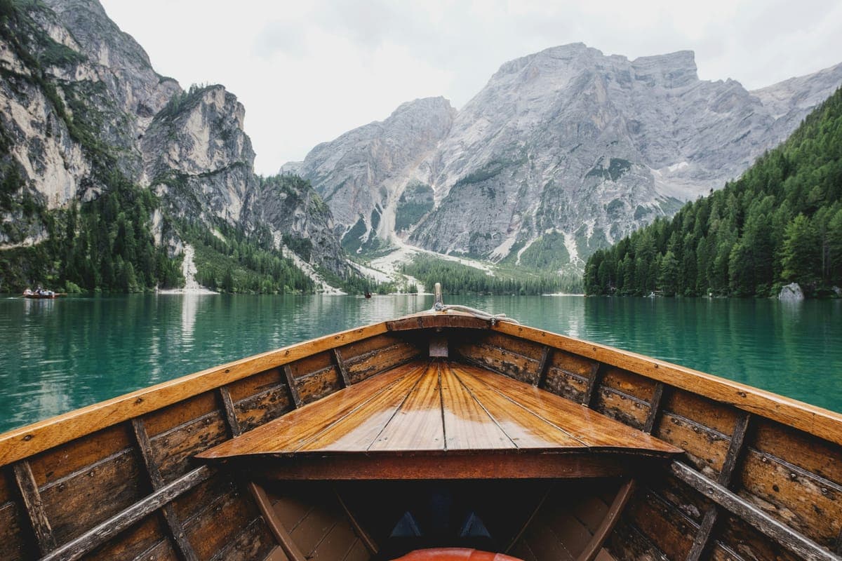 The bow of a wooden boat on a turquoise lake below mountains