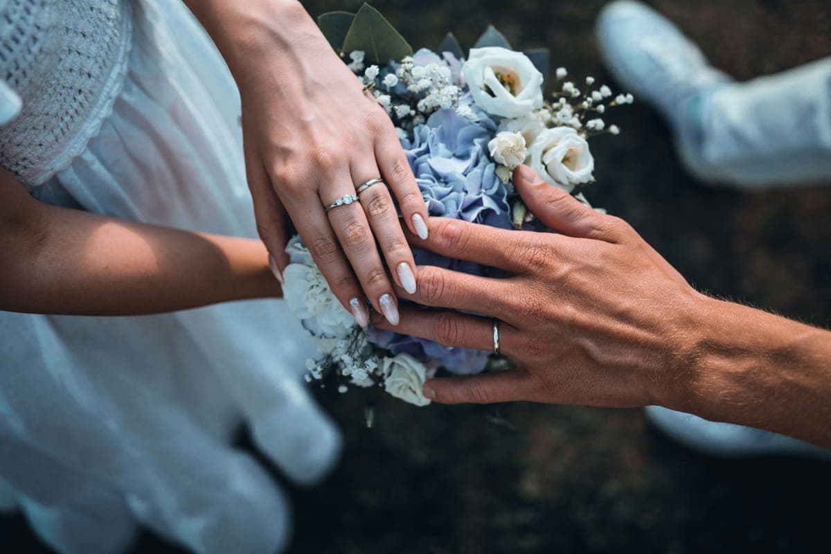A couple's hands with wedding rings over a bouquet